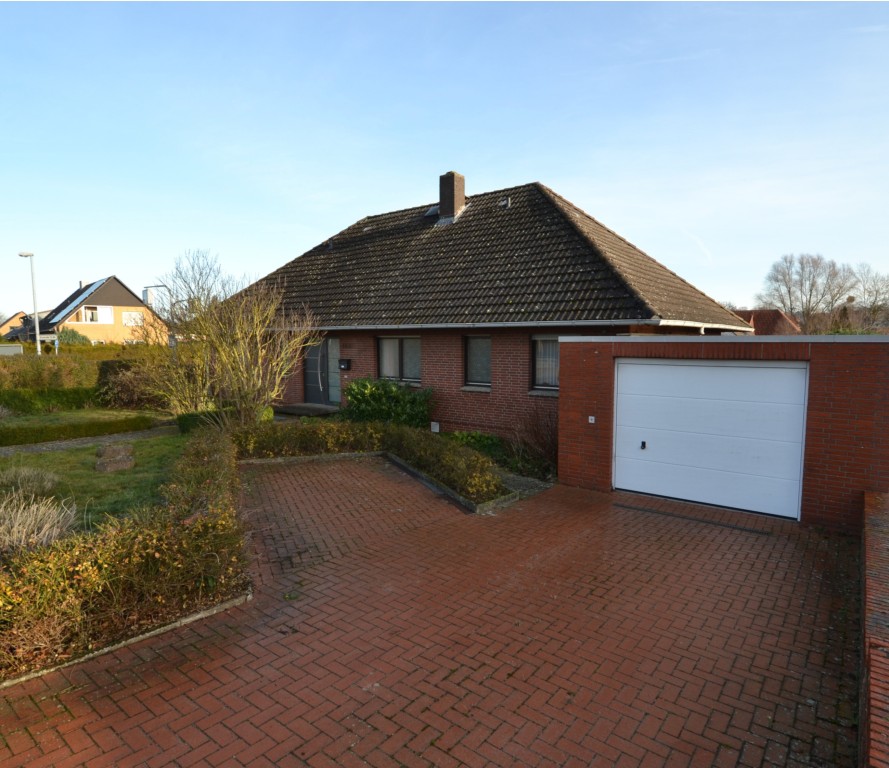 Einfamilienhaus mit Garage, rotem Ziegelmauerwerk und gepflastertem Hof an sonnigem Tag.