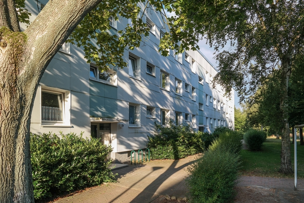 Mehrgeschossiges Wohnhaus mit Bäumen und Grünflächen in ruhiger Wohngegend bei Sonnenschein.