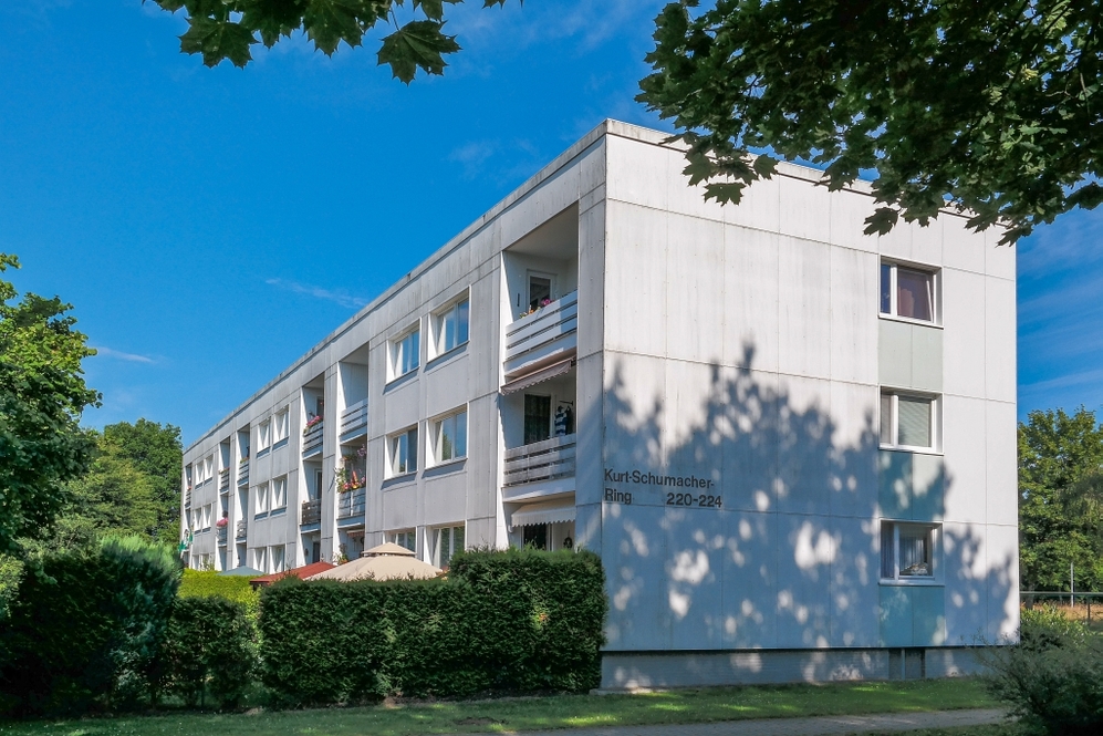 Mehrgeschossiges Wohngebäude mit Balkonen und grüner Umgebung bei klarem Himmel.