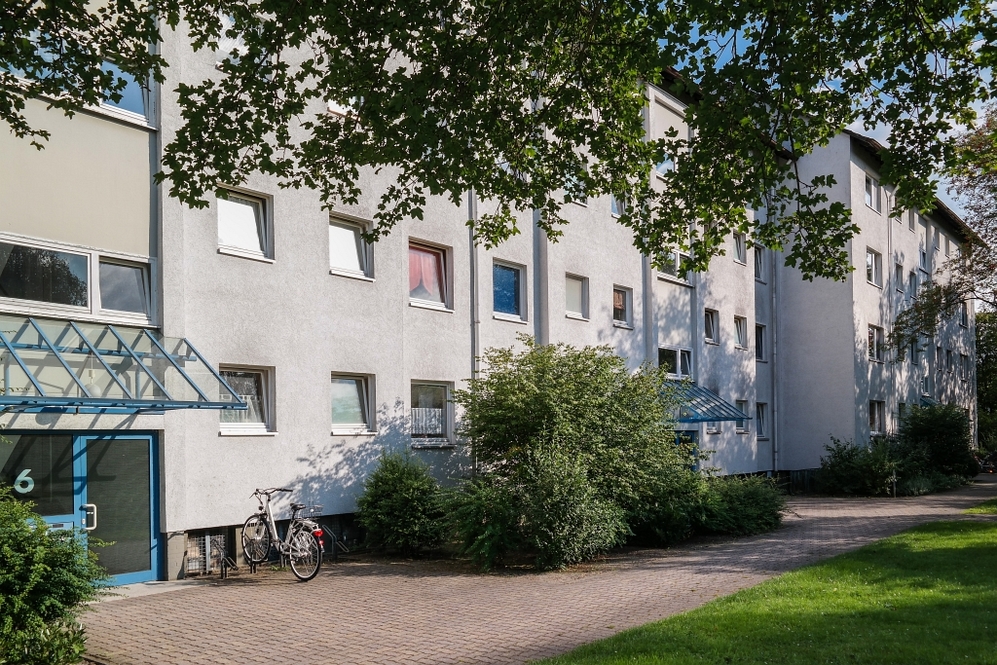 Mehrfamilienhaus mit weißer Fassade, blauen Hauseingängen und begrüntem Vorgarten.