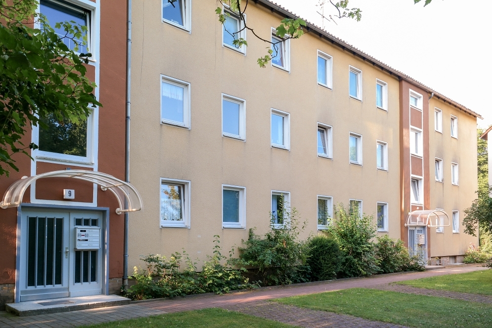 Mehrfamilienhaus mit beige Fassade, mehreren Fenstern und begrüntem Vorgartenweg.