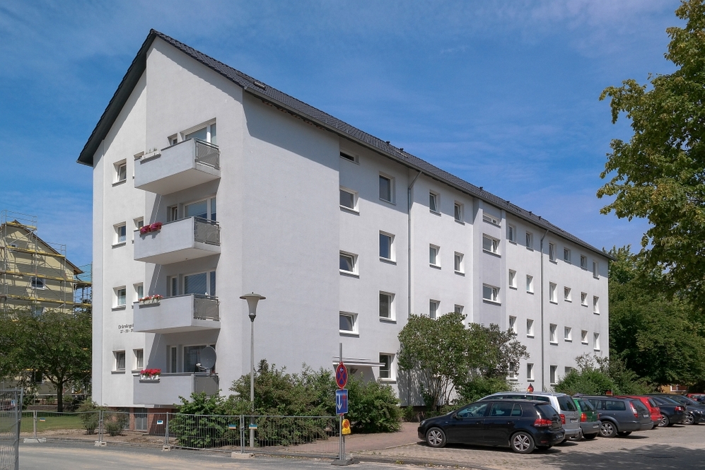 Mehrstöckiges weißes Wohngebäude mit Balkonen und Parkplatz bei klarem Himmel.