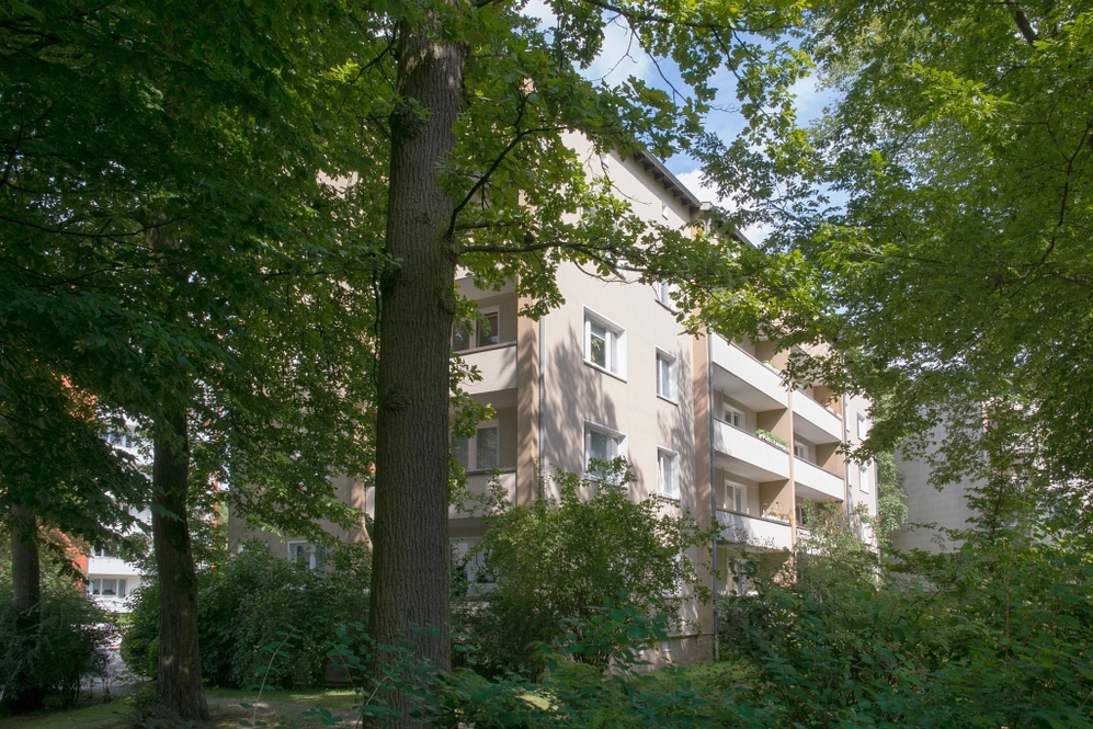 Mehrstöckiges Wohngebäude mit Balkonen, umgeben von großen Bäumen und Grünflächen.
